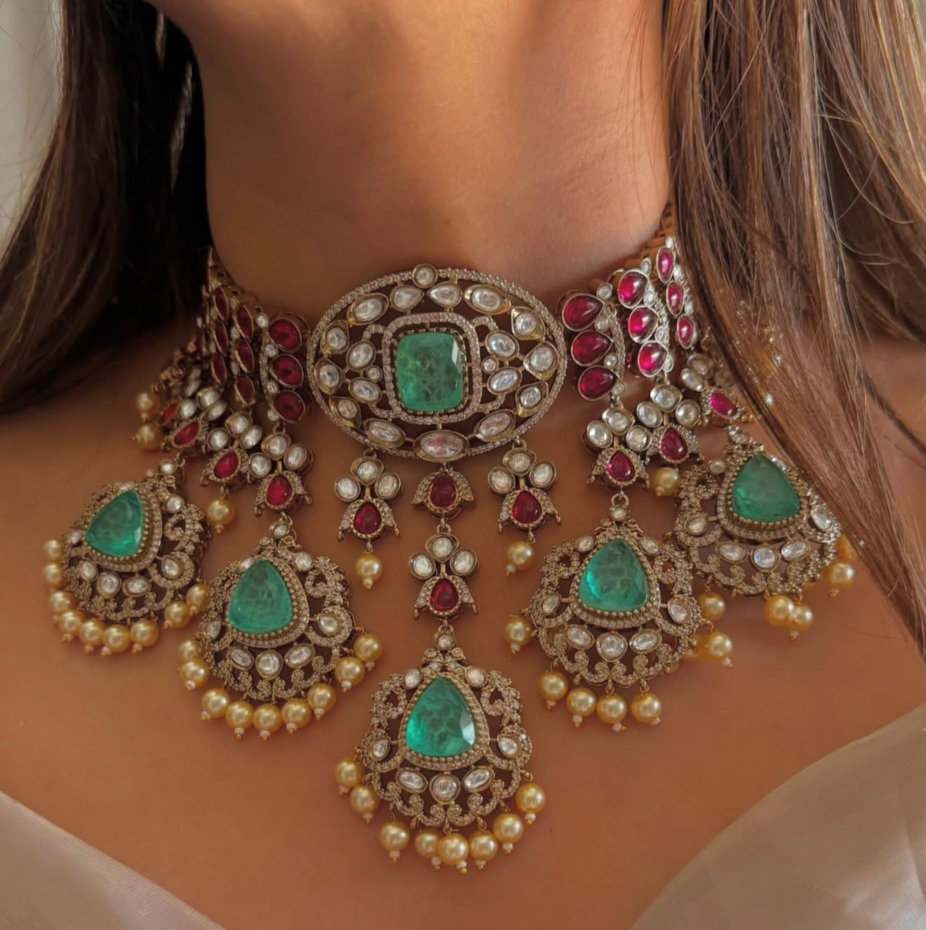 This is a Sabyasachi-inspired bridal choker set with ruby and emerald stones, and pearl hangings.