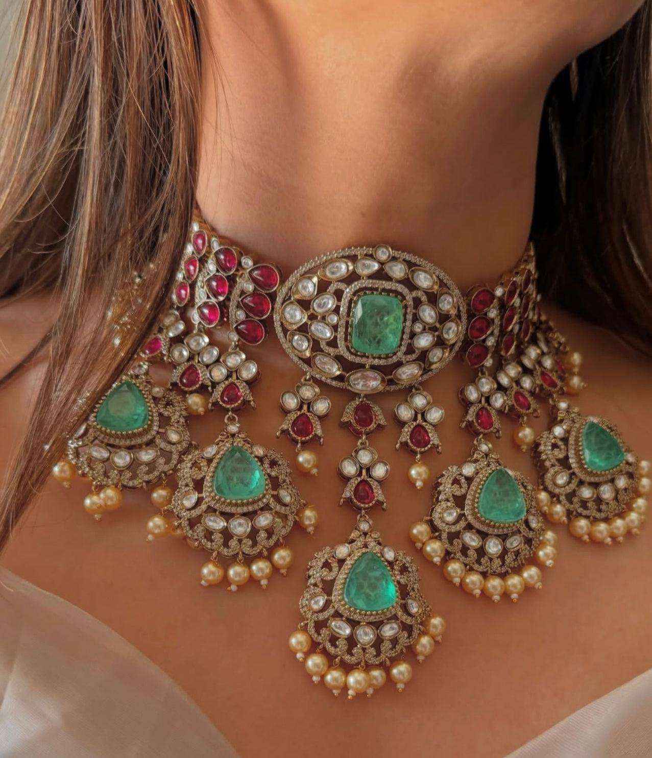 This is a Sabyasachi-inspired bridal choker set with ruby and emerald stones, and pearl hangings.